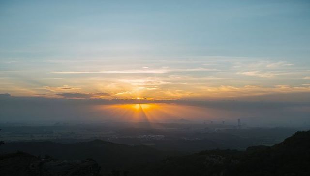 Sunrise rays spreading across misty valley from mountain ridge at dawn
