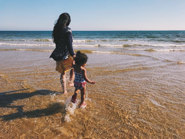 Mother and child walking on the beach by the ocean, enjoying summer vacation. Perfect for use in family-oriented content, travel magazines, and summer holiday promotions.