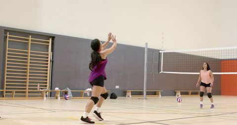 Female volleyball players setting and receiving ball on indoor hardwood court during training