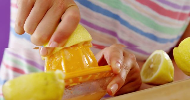 Hands squeezing lemon on manual juicer with striped shirt background. Ideal for content about healthy living, fresh beverages, natural ingredients, home cooking, culinary activities, and summer refreshments.