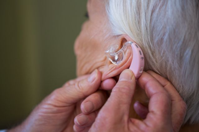 Close-up of a doctor adjusting a hearing aid for a senior patient. Useful for healthcare, audiology, elderly care, and medical technology themes. Ideal for articles, brochures, and websites focusing on hearing loss treatment and senior support.
