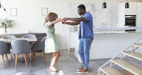 Couple dancing playfully in sunlit modern kitchen holding hands by marble island