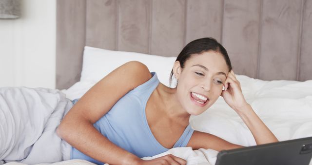 Depicting a woman in a casual setting, smiling and happily chatting online. Perfect for illustrating themes related to online communication, remote work, relaxation, and leisure activities. Ideal for blogs, websites, or advertisements focusing on technology use, home comfort, telecommuting, and positive lifestyle habits.