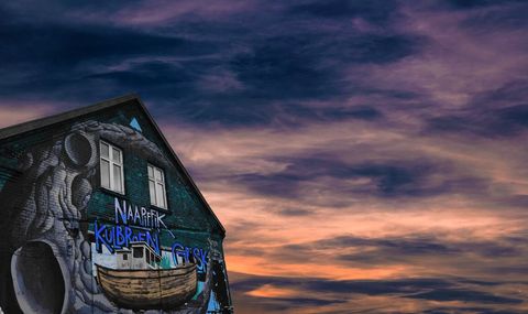 Urban mural boat on gable wall against dramatic purple orange sunset sky, coastal vibe