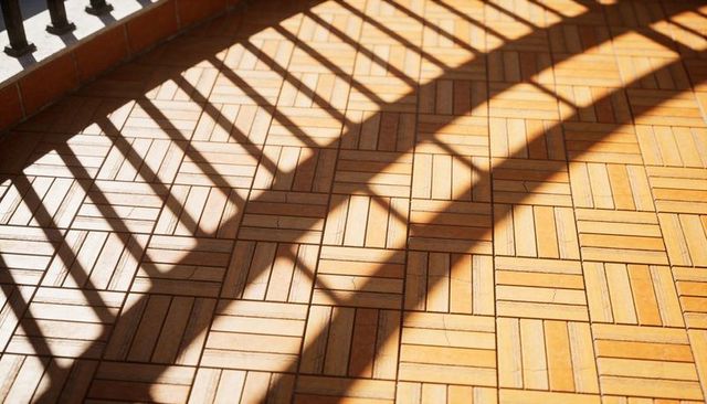 Sunlight Casting Diagonal Metal Railing Shadows on Woven Wooden Parquet Balcony Floor