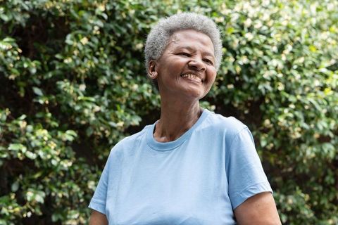 Senior african american woman smiling in sunlit backyard garden, wellness portrait