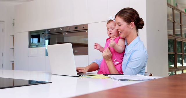 Working Mother Holding Baby While Using Laptop in Modern Kitchen - Download Free Stock Images Pikwizard.com