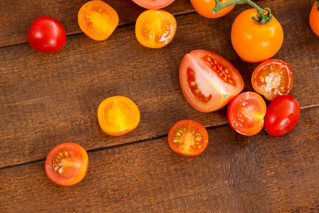 A colorful assortment of fresh tomatoes displayed on a wooden surface. The variety includes red, yellow, and orange tomatoes, some of which are sliced to reveal their juicy interiors. This image is perfect for use in food blogs, healthy eating promotions, organic vegetable advertisements, or cookbooks.