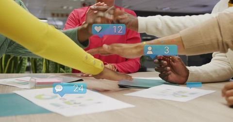 Multicultural Team Stacking Hands Over Desk Displaying Social Media Notifications and Project Charts