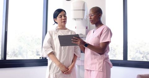 Breast clinic nurse explaining mammography results on tablet to patient in gown