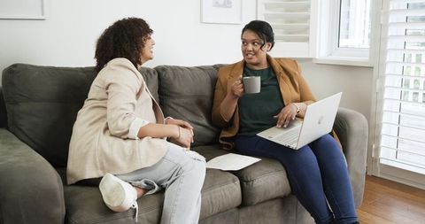 Female colleagues collaborating on sofa with laptop and coffee in bright home office
