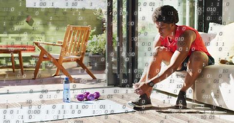 Man tying sneaker before home workout in sunlit living room with mat and dumbbells