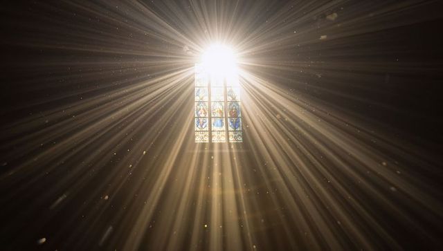 Sunbeams streaming through stained glass window in historic chapel nave dust motes glowing