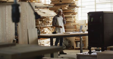 Male Carpenter Using Smartphone in Industrial Workshop