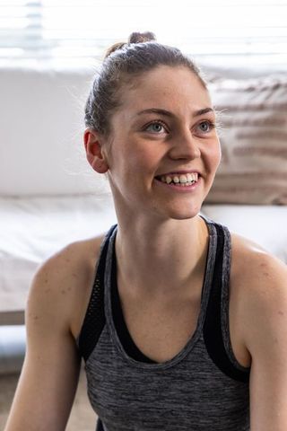 Young woman relaxing after workout at home wearing tank and sports bra, smiling naturally