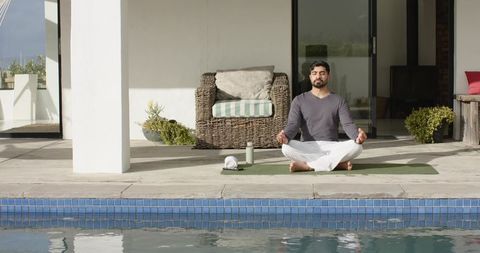 Indian man meditating poolside on green yoga mat for wellness and relaxation