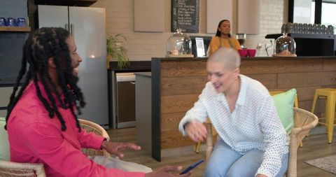 Diverse friends sharing smartphone and laughing in cozy cafe with barista in background