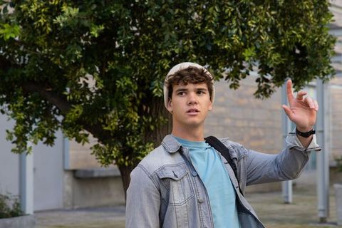 Teenager wearing denim jacket and beanie raising fingers and looking up in urban courtyard