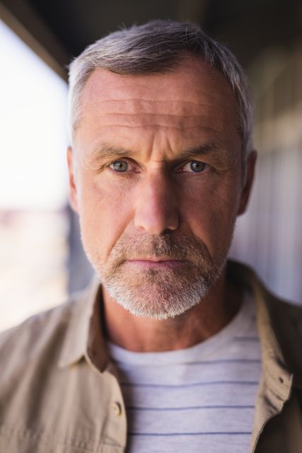 This image features a close-up portrait of a mature businessman with grey hair and a beard, standing in an office environment. His serious and focused expression conveys professionalism and confidence, making this image suitable for corporate websites, business presentations, leadership articles, and professional profiles.