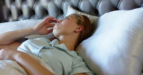 Young woman lying in bed touching face and gazing beside tufted leather headboard