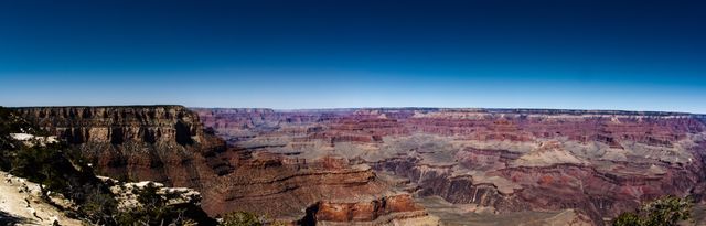 Panoramic view of the Grand Canyon under a clear blue sky illustrating the vast and rugged landscape. This image captures the natural beauty and geological features that make the Grand Canyon a famous travel destination. Suitable for travel magazines, nature blogs, educational content on geology, or promotional material for tourism and national parks.