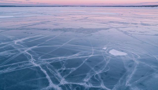Frozen lake surface with crisscrossing ice cracks at sunrise