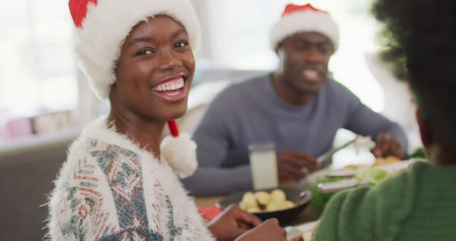 Smiling family enjoying a festive Christmas dinner while wearing Santa hats. Perfect for promoting holiday celebrations, family gatherings, and joyful festive moments. Useful for advertising holiday events, festive greeting cards, and seasonal promotions emphasizing togetherness and happiness during the Christmas season.