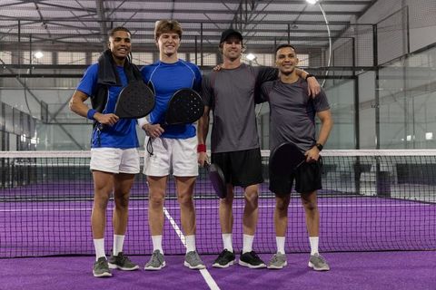 Four male padel players posing on indoor purple court displaying team camaraderie