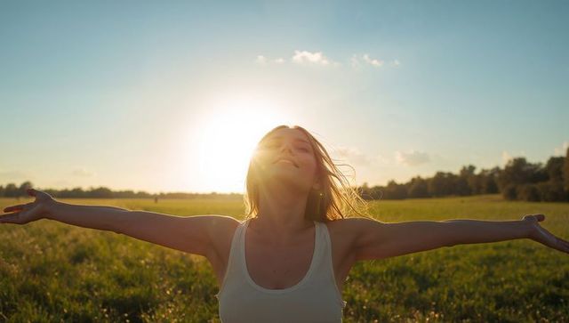 Young Woman Embracing Sunlight in Meadow During Golden Hour with Outstretched Arms