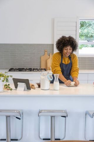 African american woman kneading dough on modern kitchen island using tablet for recipe