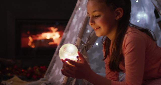 Girl holding glowing ball in cozy homemade tent near fireplace - Download Free Stock Images Pikwizard.com