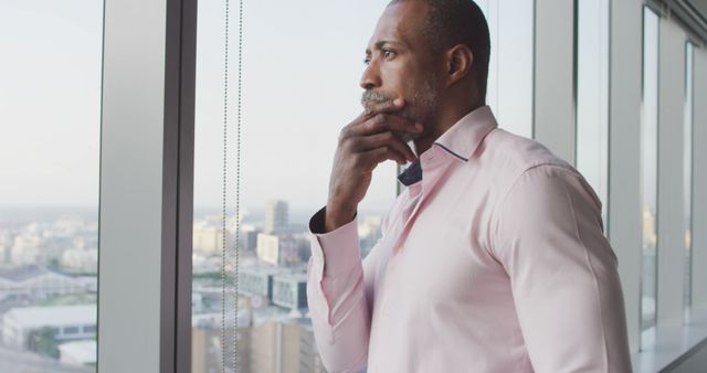 Depicting a businessman in deep thought, looking out of a high-rise office window over the cityscape. Ideal for themes such as business planning, corporate decision-making, career development, and urban professional life. Could be used in blog posts about business strategies, executive training, or professional growth.