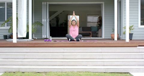 Mature woman meditating on porch yoga mat practicing mindfulness with light dumbbells