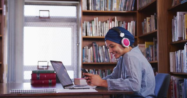 Young Woman Wearing Headphones Studying in Library with Laptop and Smartphone - Download Free Stock Images Pikwizard.com