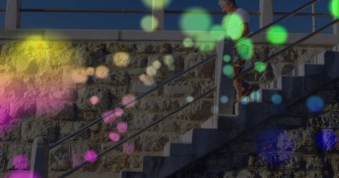 Senior man descending sunlit stone steps with colorful bokeh and metal handrail