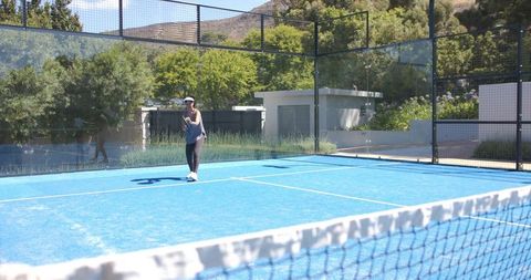 Playing padel on bright blue court with modern clubhouse, fencing and hillside greenery