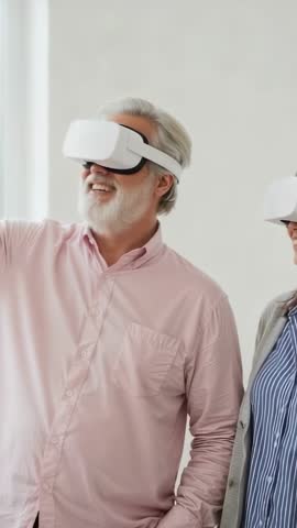 Senior man wearing VR headset laughing and pointing while partner explores virtual world