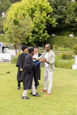 Diverse graduates celebrating with mentor on lawn at outdoor campus graduation ceremony