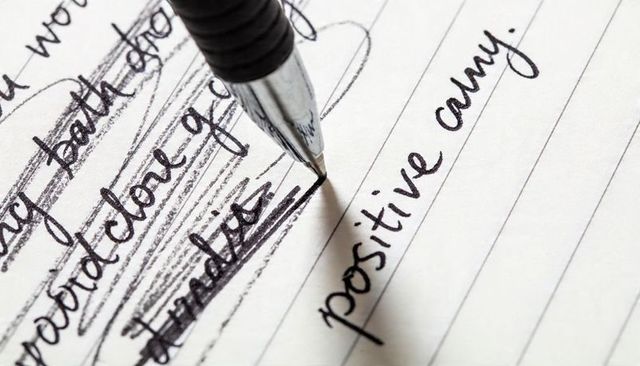 Ballpoint pen writing positive while crossing out negative words on lined notebook page