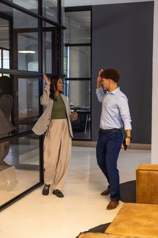 Young diverse coworkers giving high-five in modern office hallway near glass partitions