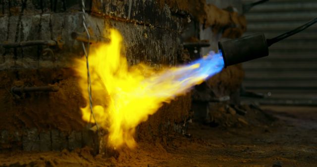 Close-up of industrial blowtorch producing blue and yellow flame. Ideal for content about welding, metalwork, and industrial manufacturing processes. Suitable for illustrating themes related to engineering, fabrication, and flame-based applications. Can be used in educational and informative materials on combustion and heat generation in industry.