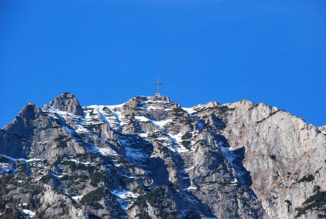 Snow-capped mountain peak featuring prominent cross under clear blue sky. Ideal for use in travel blogs, religious content, posters, inspirational materials, and outdoor adventure advertisements.