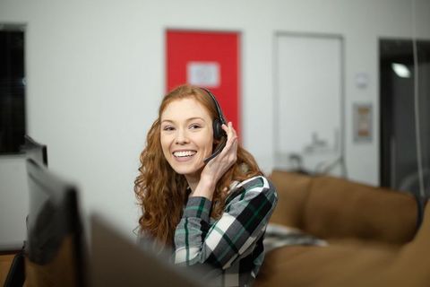 Smiling Professional Woman in Home Office Adjusting Headset