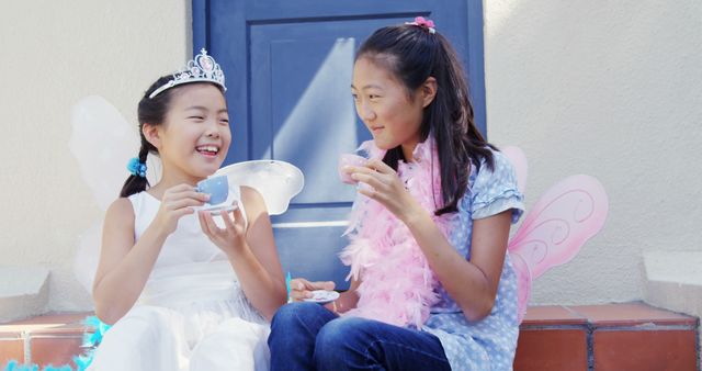 Two Asian girls enjoy a playful moment outdoors, dressed in fairy costumes. Their laughter and costumes add a whimsical touch to a sunny day.