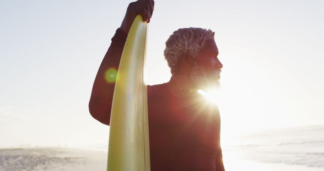 Senior african american man holding surfboard on sunny beach. healthy and active time beach holiday.