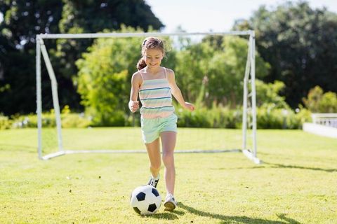 Energetic girl playing soccer in bright sunny backyard