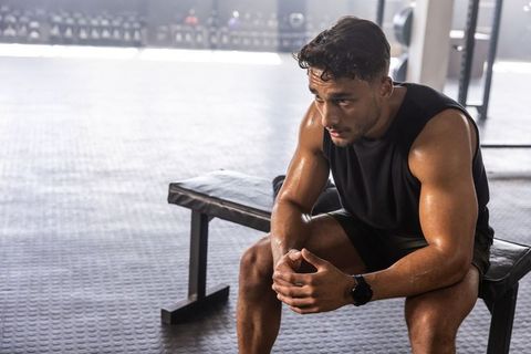 Muscular man resting on gym bench after intense strength training, focused