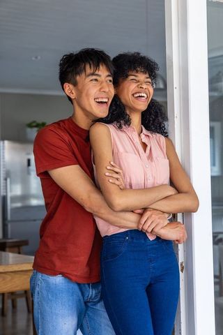 Laughing couple embracing in bright modern kitchen doorway, natural light, casual home moment