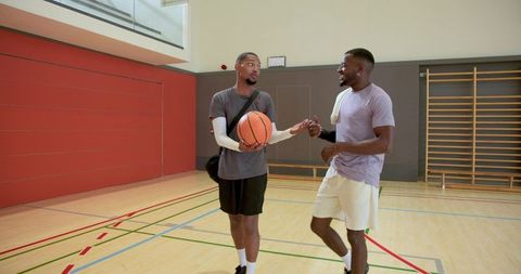 African american friends walking gym court holding basketball, sharing team bonding