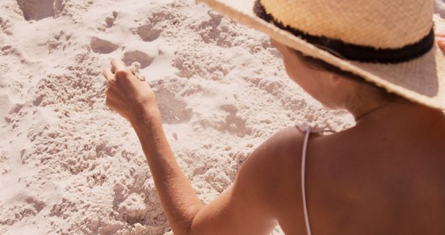 A woman in a straw hat enjoys a serene moment drawing in the sand on a sunny beach. - Download Free Stock Photos Pikwizard.com